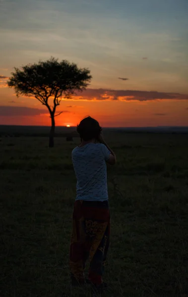 A vertical shot of a person in the field in front of a tree at scenic sunset