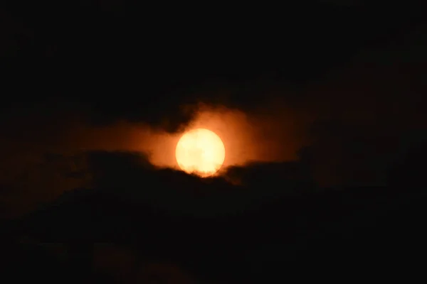 暗い雲に囲まれた空の明るいオレンジ色の月 — ストック写真