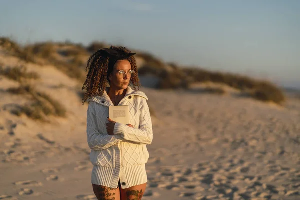 An attractive female with tattooed and a cozy cardigan walking on a beach