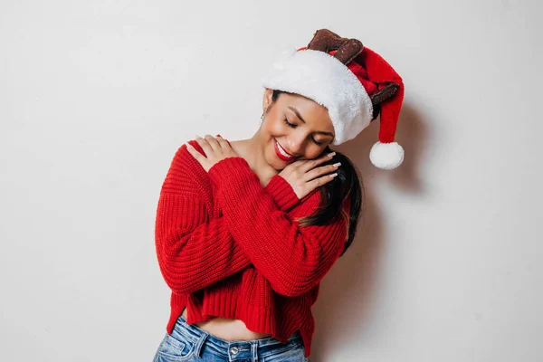 Happy Hispanic Woman Red Sweater Christmas Hat Hugging Herself Self — стоковое фото