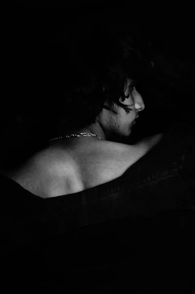 一个穿着珠宝珠宝的年轻男子在一间黑暗的房间里摆姿势的灰白照片 — 图库照片
