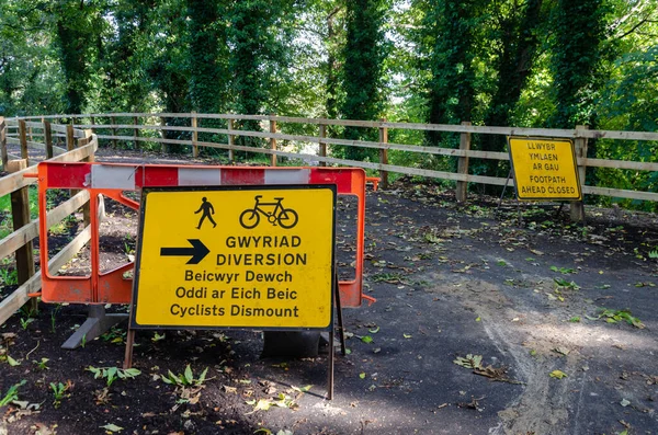 Two yellow signs placed outdoors in English and Welsh saying \'Footpath ahead closed\
