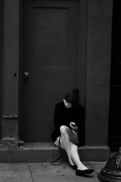 一位年轻女子坐在门阶上用手捂住脸的灰白照片 — 图库照片