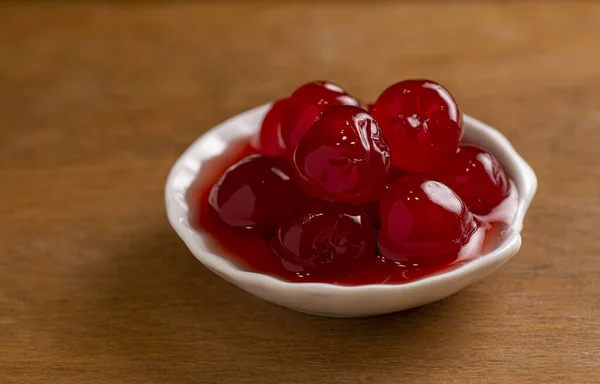 maraschino cherries in a small porcelain bowl on a wooden base