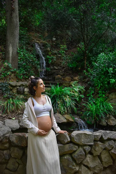一位漂亮的年轻白人孕妇 身穿白衣 在大自然中摆姿势 靠着石墙 — 图库照片