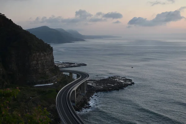 日の出の間に崖や海に囲まれた道路の風景 — ストック写真