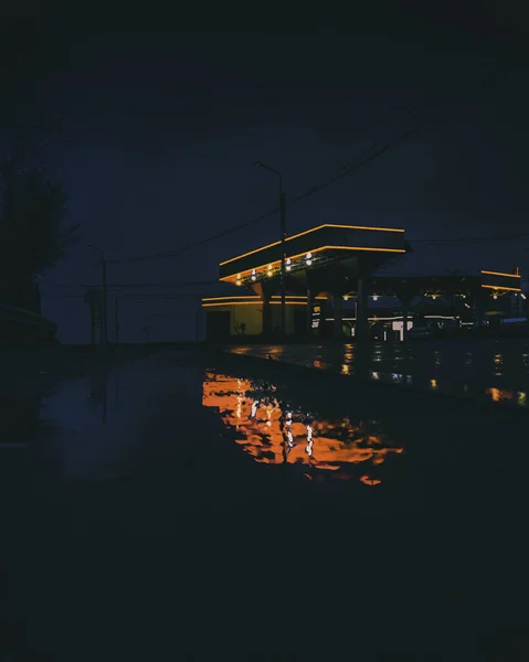 在日出前的清晨 加油站明亮的灯光映照在湿湿的街道上 — 图库照片