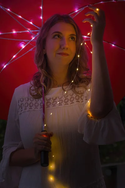 一个白种人女人拿着一把红色的伞 上面挂着彩灯 — 图库照片