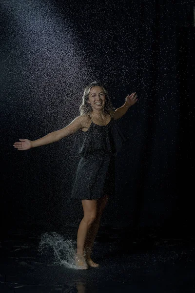 黒のドレスを着て水を楽しんでいる濡れた髪を持つセクシーな女性は暗いスタジオでスプラッシュ — ストック写真