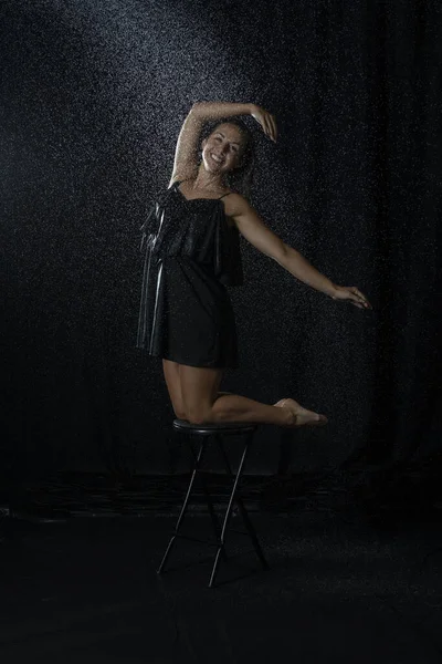 黒いドレスを着た濡れた髪をしたセクシーなダンサーと暗いスタジオで水の飛沫を楽しむ — ストック写真