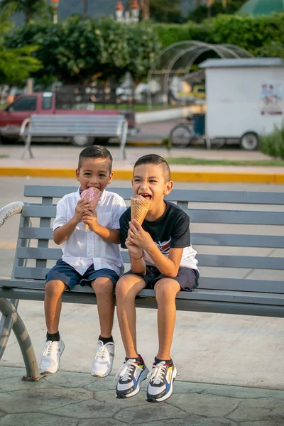 Dwoje Latynosów Wesołych Dzieciaków Siedzących Ławce Parku Jedzących Lody — Zdjęcie stockowe