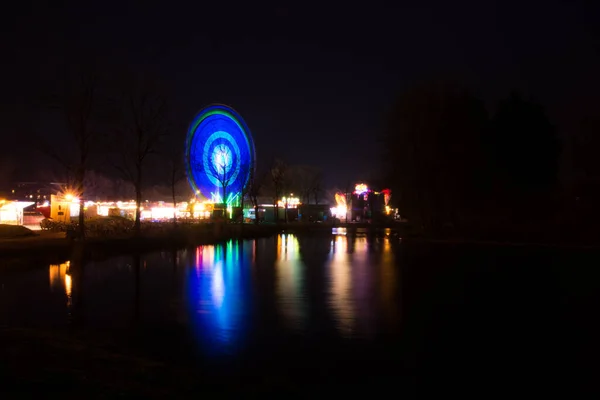 ライトアップされた公園内の観覧車と夜の反射湖 — ストック写真