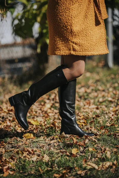 秋の葉を歩きながら黒いファッショナブルなブーツを着た女性 — ストック写真