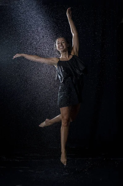 黒いドレスを着た濡れた髪をしたセクシーなダンサーと暗いスタジオで水の飛沫を楽しむ — ストック写真