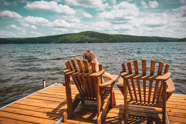 A person resting on a folding chair on a wooden dock on the sea under a cloudy sky and sunlight