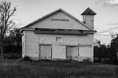A grayscale of the old capote baptist church on the grassy field in Texas clipart