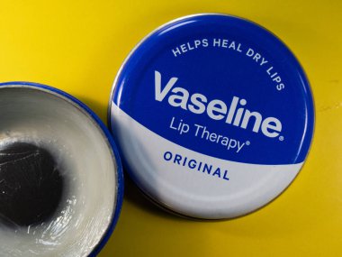 MANCHESTER, UNITED KINGDOM - Nov 21, 2021: Open tin of vaseline lip cream on a yellow backgroun clipart