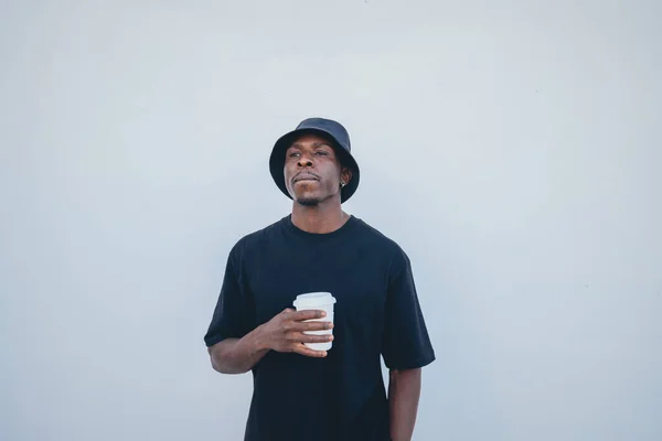 A young black man in street-style clothes holding his takeaway drink on a white background
