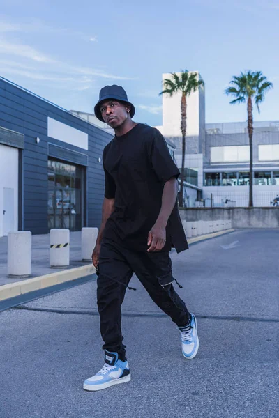 自信を持って屋外を歩くストリートスタイルの服の若い黒人男性の垂直ショット — ストック写真
