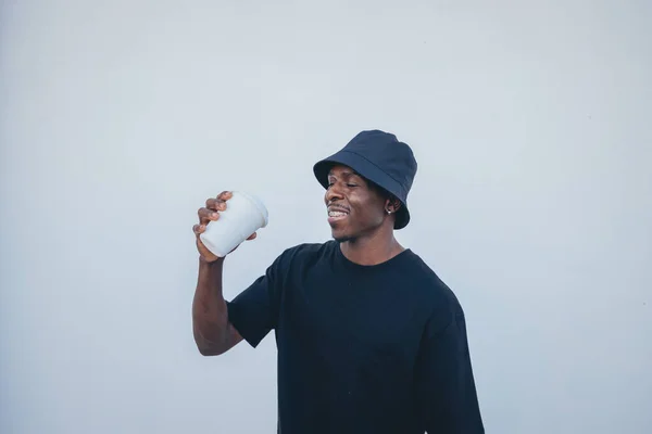 A young black man in street-style clothes happy with his takeaway drink on a white background