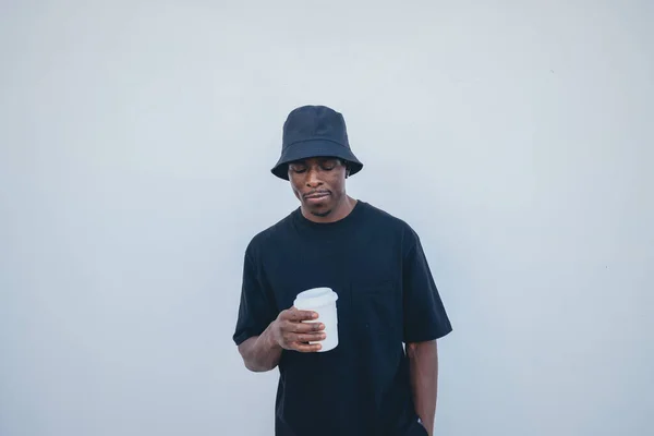 A young black man in street-style clothes holding his takeaway drink on a white background