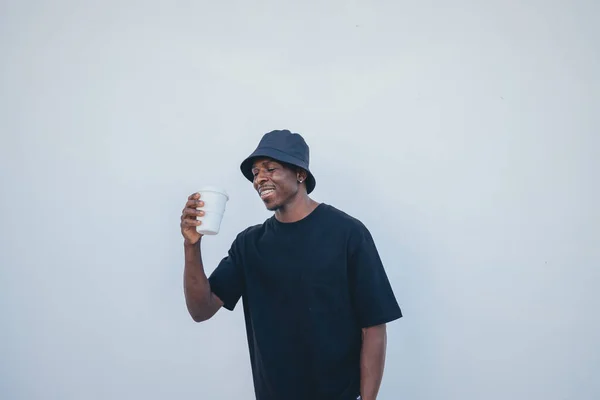 A young black man in street-style clothes happy with his takeaway drink on a white background