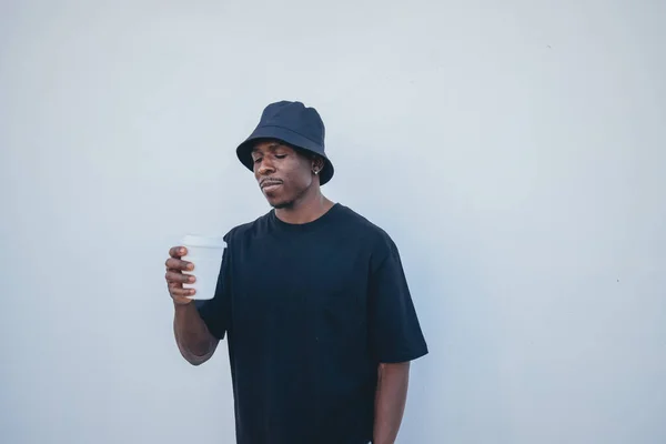 A young black man in street-style clothes holding his takeaway drink on a white background