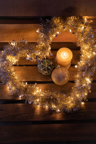 キャンドルやクリスマスボールの装飾が施された木製の背景に輝く光を持つハート型のガーランド — ストック写真