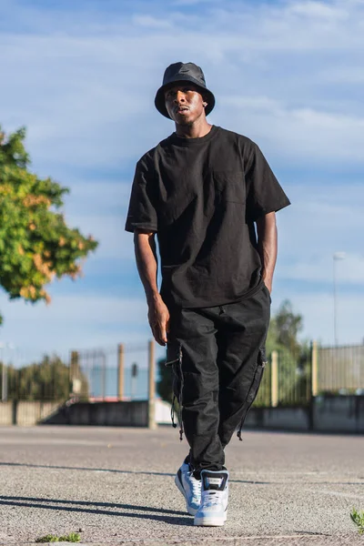 晴れた日に屋外を歩くストリートスタイルの服を着た若い黒人男性の垂直ショット — ストック写真
