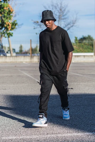 晴れた日に屋外を歩くストリートスタイルの服を着た若い黒人男性の垂直ショット — ストック写真