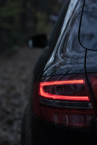 A vertical shot of a black luxurious car with an illuminated reversing light