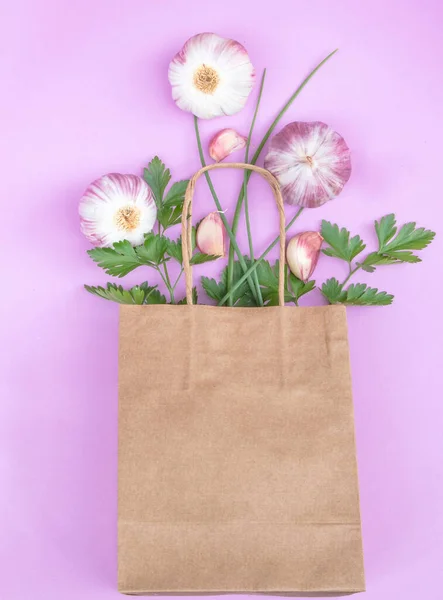 A top view of a paper bag with parsley, chives, and garlic on a purple background