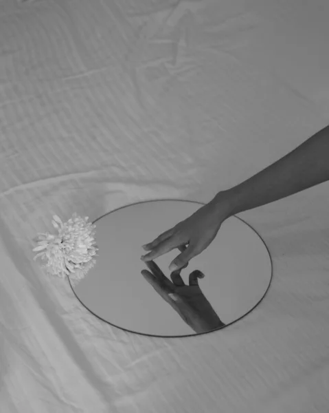 A monochrome shot of a female hand on a round mirror put on a bed