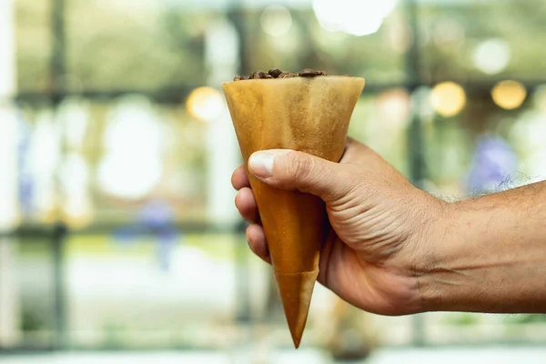 コーン型の包みに香り高い焙煎コーヒー豆を入れた手のクローズアップ — ストック写真
