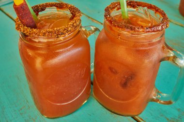 Michelada served in mason glass with tamarind candy garnish and spicy on a cyan wood background clipart