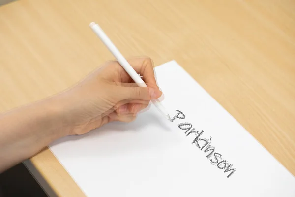 パーキンソン病の女性が震えながら白い紙に書こうとした — ストック写真