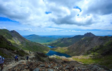The climbers are ascending Snowdon with views across Snowdonia and a mountain lake, U clipart