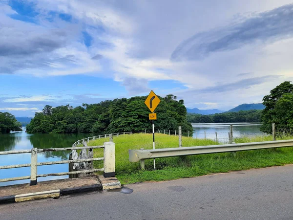 Yellow Right Curve Road Sign Pole Lake Blue Cloudy Sky — Stockfoto