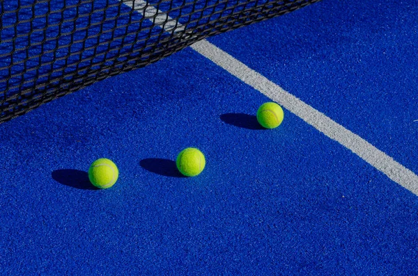 Three paddle tennis balls next to the net and serbing line of a paddle tennis court.