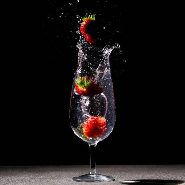 黒の背景にスプラッシュが隔離された水のガラスに落ちるイチゴのクローズアップショット — ストック写真