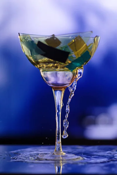 Colpo Verticale Bicchiere Cocktail Rotto Che Perde Uno Sfondo Blu — Foto Stock