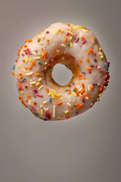 Eine Vertikale Aufnahme Eines Donuts Mit Weißem Zuckerguss Und Regenbogenbestreuungen — Stockfoto