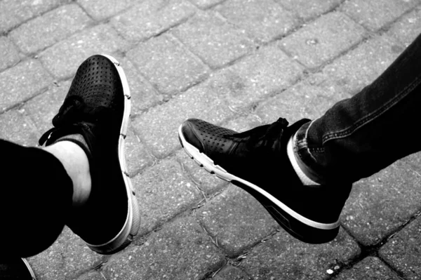 A greyscale shot of the legs of a person in black sneakers