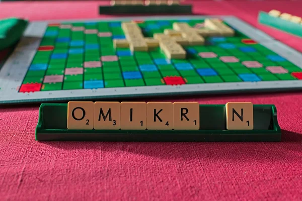 拼字游戏的代名词在棋盘前的托架上形成单词Omikron 上面有红色桌布 — 图库照片