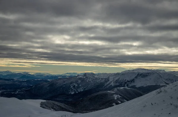 Ett Landskap Steniga Kullar Täckt Snö Solljuset Och Molnig Himmel — Stockfoto