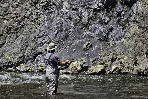 岩の多い崖に対して川で釣りをする漁師 — ストック写真