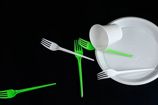 The plastic disposable forks, plate, glass are on a black background. picnic set.