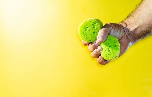 Closeup Shot Male Hand Squeezing Green Sponge Illuminated Yellow Background — Stockfoto