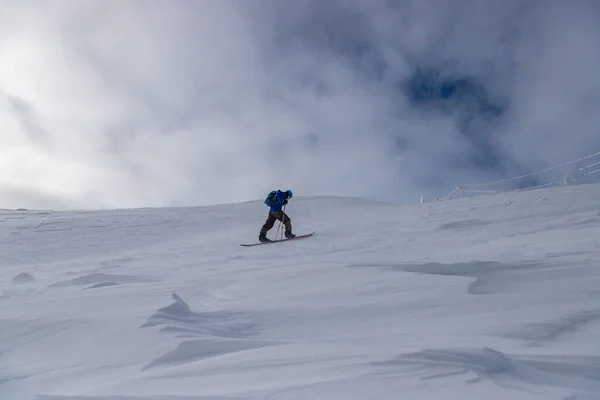 在多云的天空和阳光下 一个成年人在雪山上滑行滑雪地 — 图库照片