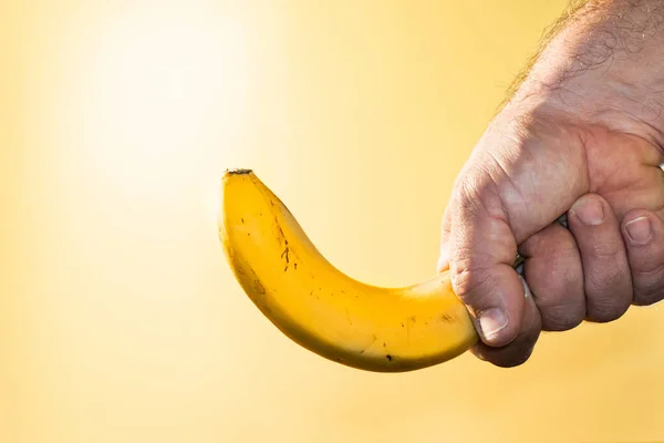 Zbliżenie Ujęcia Męskiej Ręki Trzymającej Banana Podświetlanym Żółtym Tle — Zdjęcie stockowe